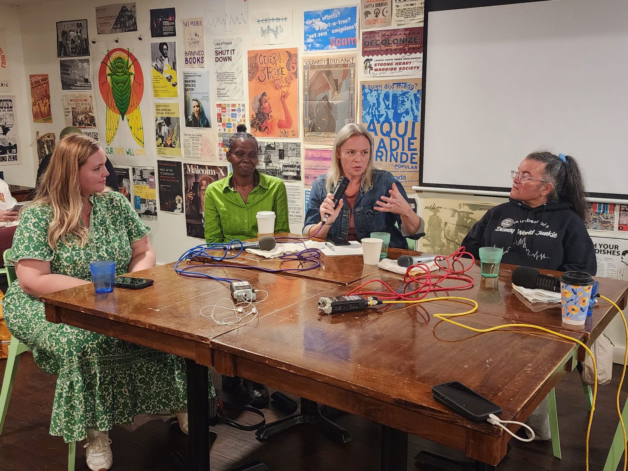 Hilary Flint (left), Melanie Meade (left-center), Elise Keaton Wade (right-center), and Angela Shaneyfelt (right) sit together at a table during a "Working People" live show panel hosted at Red Emma's bookstore in Baltimore on Oct 19, 2024. Photo by Maximillian Alvarez.