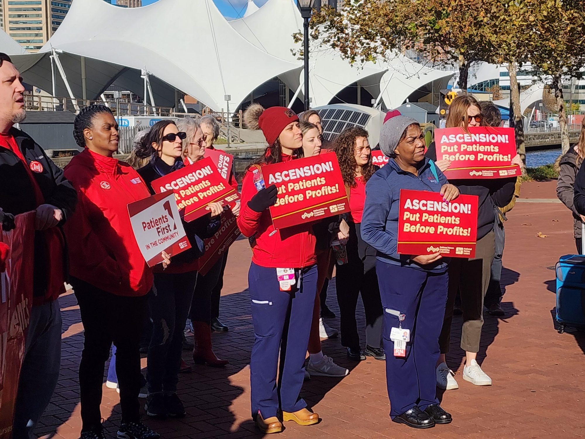 Unionized nurses at Ascension St. Agnes Hospital stand together at a rally held in downtown Baltimore on Nov. 12, 2024, holding signs that say, "Ascension! Put patients before profits!" Photo by Maximillian Alvarez.