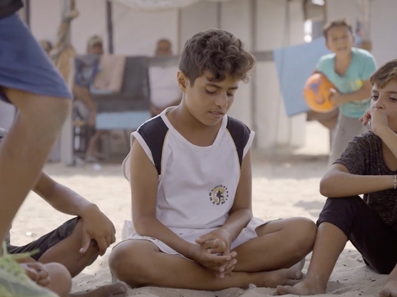 Children sit in the shade in a refugee camp in Khan Younis. Frame from video shot by Ruwaida Amer.