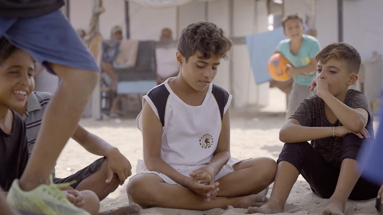 Children sit in the shade in a refugee camp in Khan Younis. Frame from video shot by Ruwaida Amer.