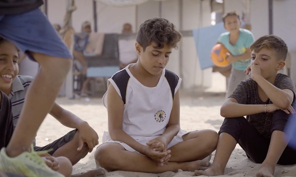 Children sit in the shade in a refugee camp in Khan Younis. Frame from video shot by Ruwaida Amer.