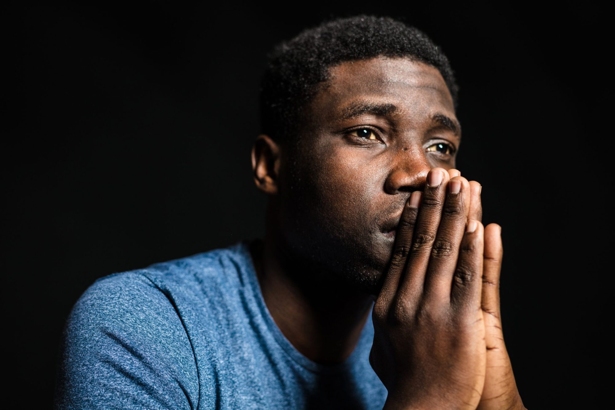 Young man looking away with hands clasped. Photo via Getty Images