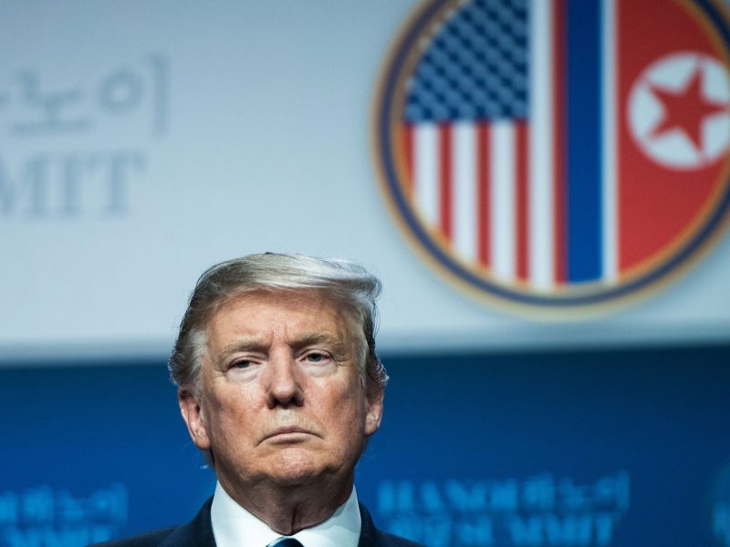 Profile of Donald Trump's face. He is standing in front of an emblem featuring the flags of the US and the DPRK.