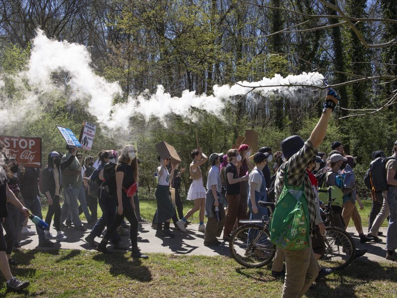 Cop City Atlanta protesters move in a crowd in the Weelaunee Forest in Atlanta. One protestor holds up burning sage, the smoke trail can be seen over the protesters' heads.