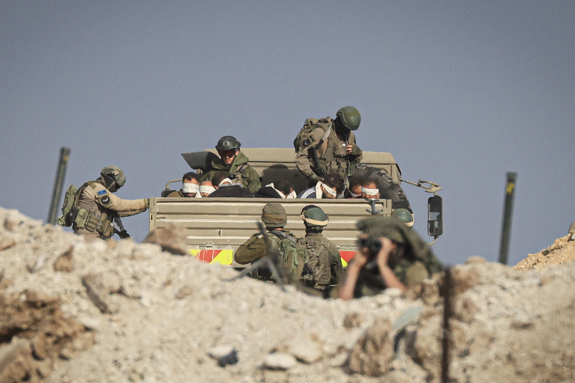 Israeli soldiers detain blindfolded Palestinian men in a military truck while watching Palestinians (not pictured) fleeing the fighting in war-torn Gaza walk by on a road in the Zeitoun district of the southern part of the Gaza Strip on November 19, 2023. Photo by MAHMUD HAMS/AFP via Getty Images