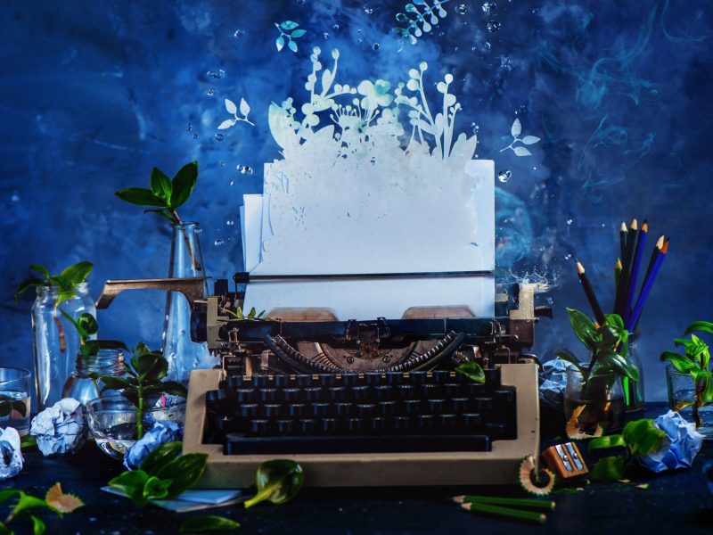 Creative writer workplace with a typewriter and growing plants. Imagination garden concept. Dark still life with action and copy space. Photo via Getty Images