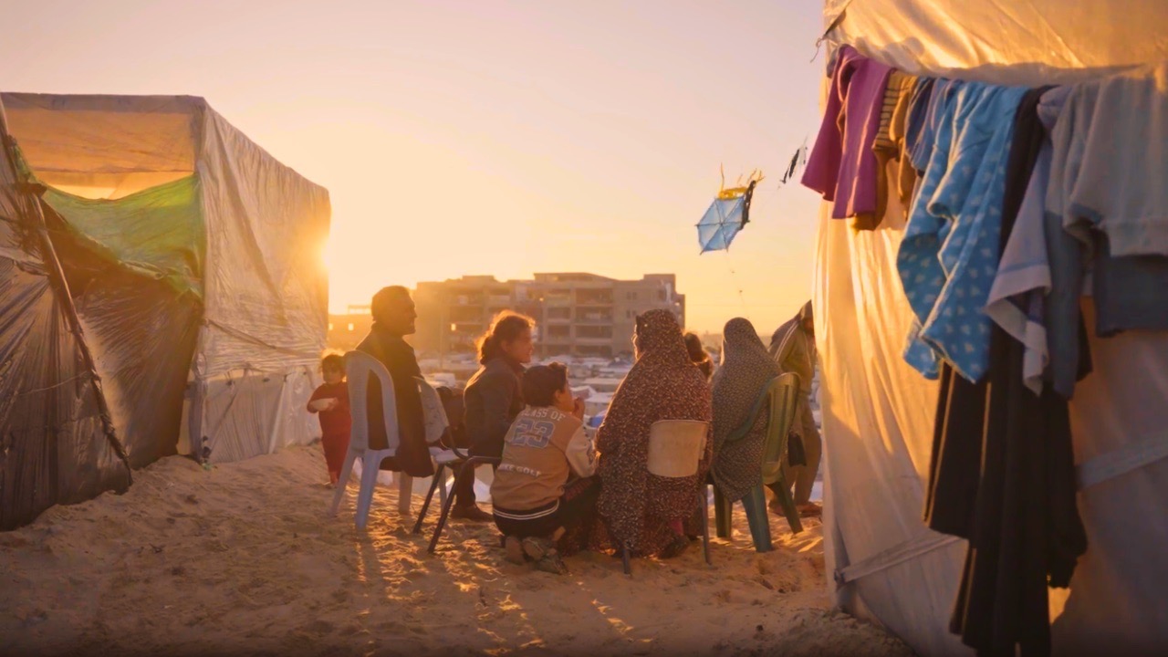 A family in Gaza shares a brief moment together at sunset outside of their tent in a makeshift refugee camp. Screenshot from video by Ruwaida Amer